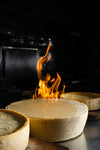 Cheese wheel being heated with a flame in a dark setting